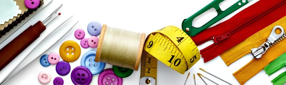 Assorted sewing supplies including thread spool, colorful buttons, measuring tape, zippers, scissors, and fabric swatches laid out.