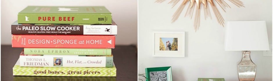 Stack of colorful cookbooks on a coffee table beside a white lamp in a bright living room.