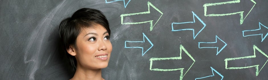 Woman looking up beside a chalkboard covered with colorful arrows pointing in different directions.