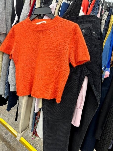 Bright orange fuzzy knit short-sleeve sweater on a hanger among racks in a store.