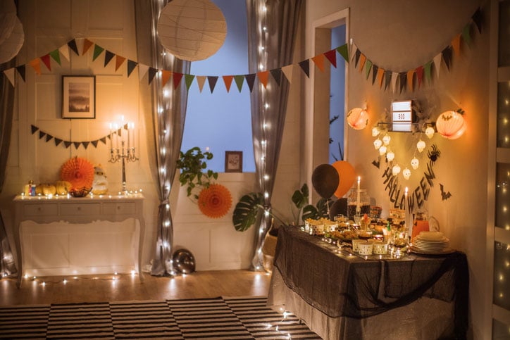 Cozy indoor Halloween party with colorful bunting, string lights, and a dessert table.