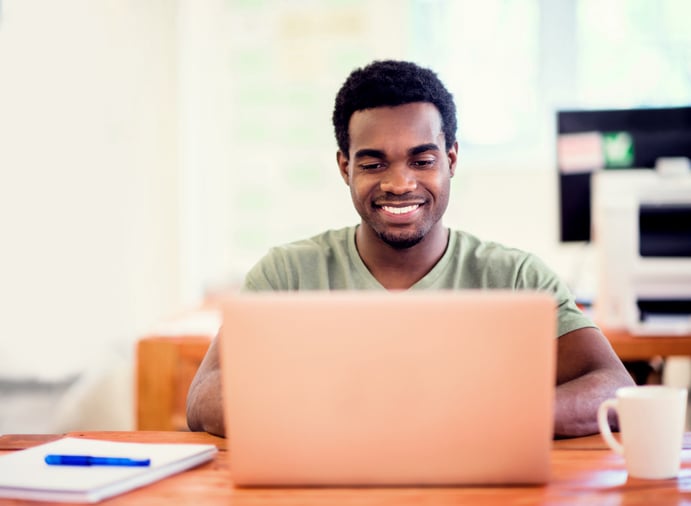 Smiling man working on a laptop at a wooden desk in a bright, modern office.