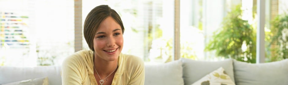 Smiling young woman sits on a light-colored sofa in a bright living room.