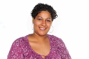 Smiling woman with short curly hair wearing a purple patterned blouse against a white background.