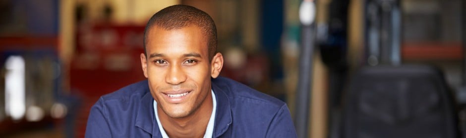 Smiling man in a blue uniform inside a workshop.