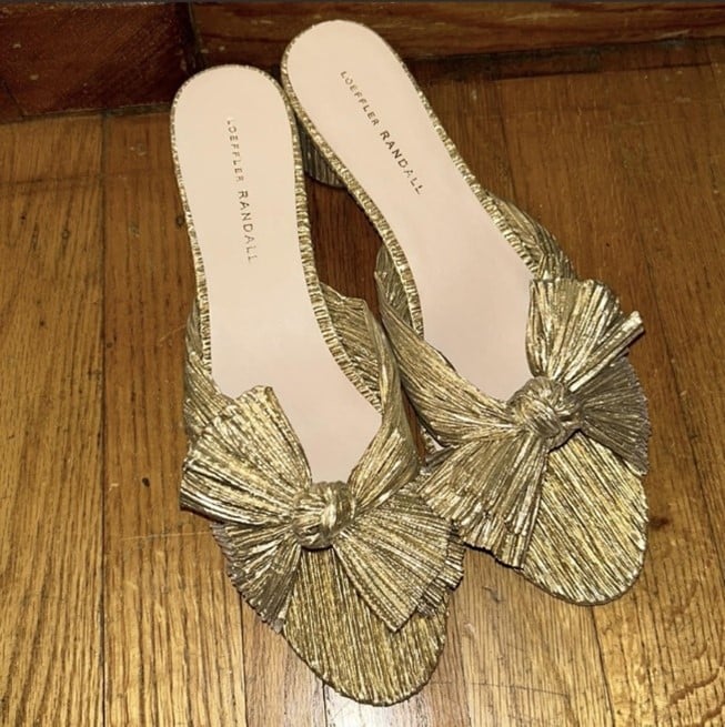 Gold metallic bow-embellished pleated mules on a wooden floor