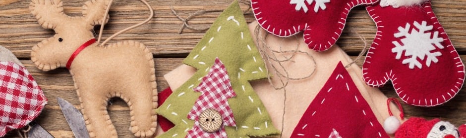 Assorted holiday felt decorations on a wooden table, including a reindeer, stitched trees, and snowflake ornaments