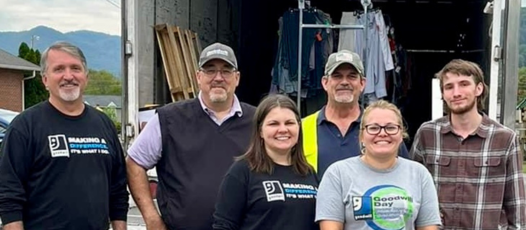 Six volunteers pose in front of a clothing donation truck outdoors.