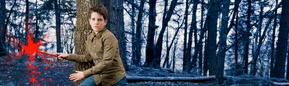 Boy in a forest pretending to cast a spell with glowing red sparks.