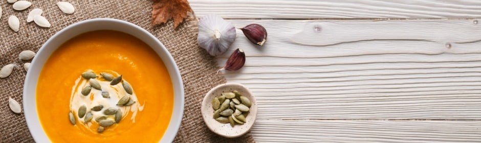 Creamy orange pumpkin soup topped with yogurt swirl and pumpkin seeds on a light wooden surface.