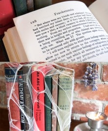 Open book above a bundle of wrapped colorful books against a brick wall.