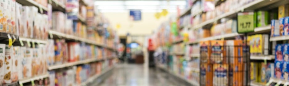 Blurred view of a grocery store aisle with shelves stocked on both sides.
