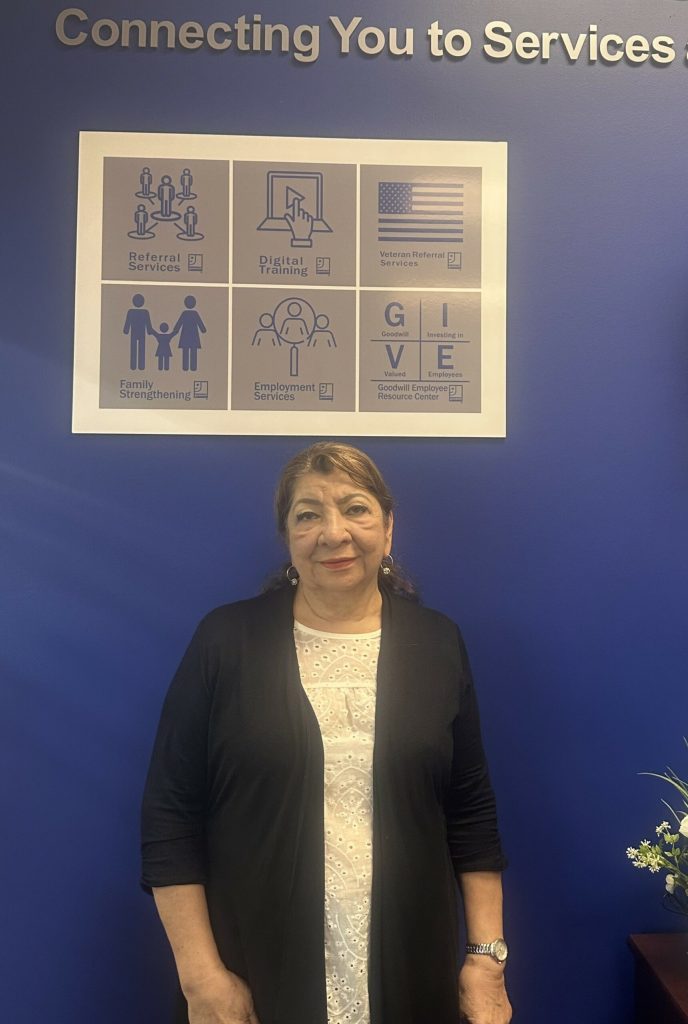 Woman standing in front of a blue wall with a six-panel poster titled Connecting You to Services.