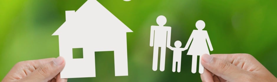 Paper cutout of a house and a family held by hands against a green, blurred background