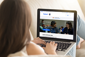 Person typing on a laptop displaying a job search homepage while relaxing on a sofa.