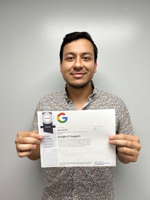 Man holding a Google IT Support certificate against a plain gray wall.