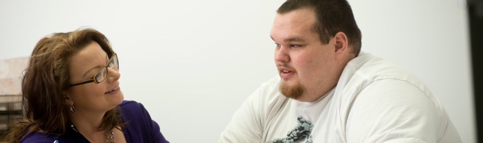 Woman with glasses converses with a man in a white T-shirt across a desk.