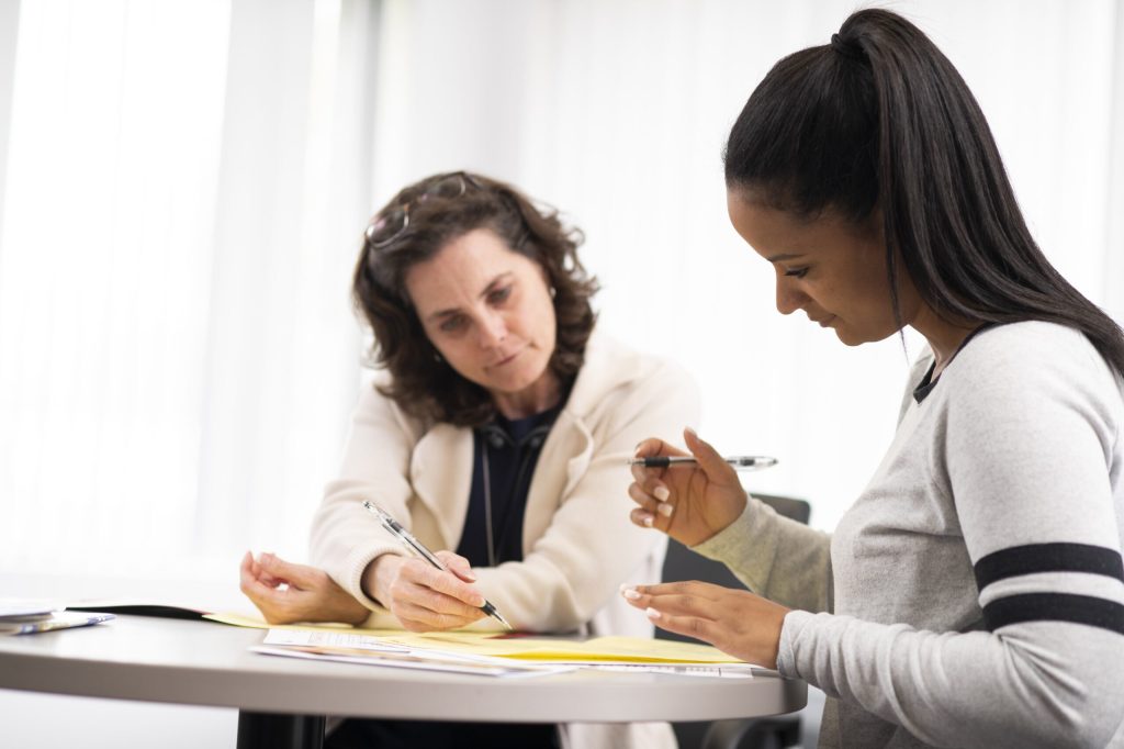 Two women review documents at a round table during a tutoring session.