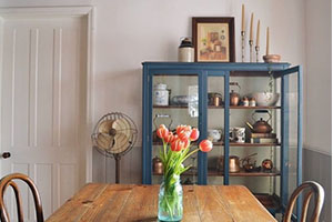 Dining room with a blue glass-front cabinet, wooden table, and a vase of orange tulips.