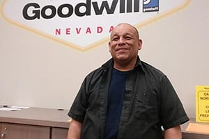 Smiling man in a dark shirt stands in front of a Goodwill Nevada sign.