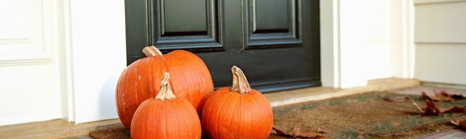 Three pumpkins on a porch near a dark front door.