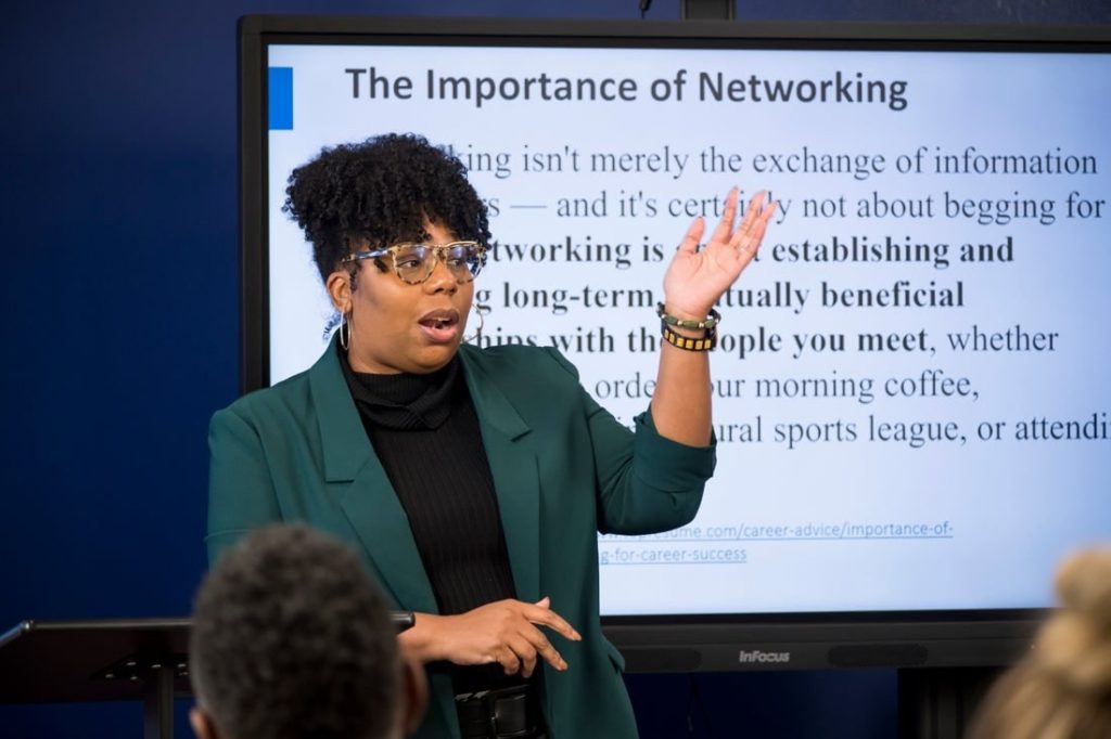 Speaker in a green blazer presenting in front of a slide titled The Importance of Networking.