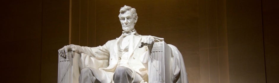 Seated white marble statue of a bearded man in a formal suit.