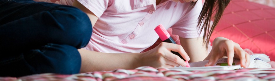 Person lying on a pink bedspread, wearing a light pink polo, writing in a notebook with a pink marker.