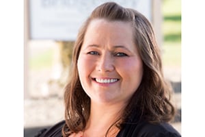 Smiling woman with shoulder-length brown hair in an outdoor setting.