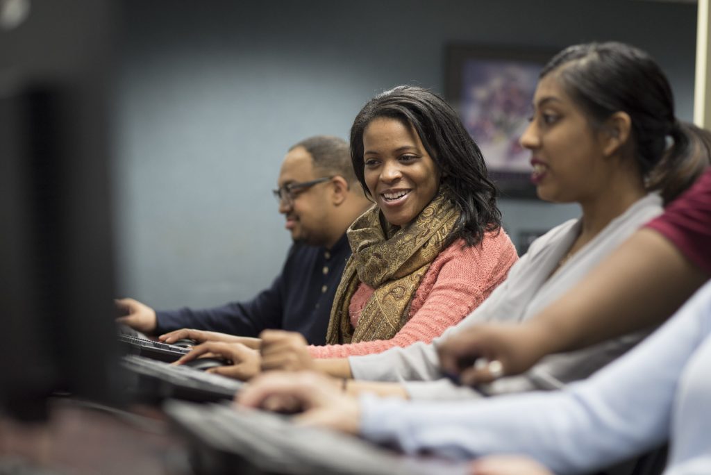 Group of adults at computers in a classroom, smiling while working.