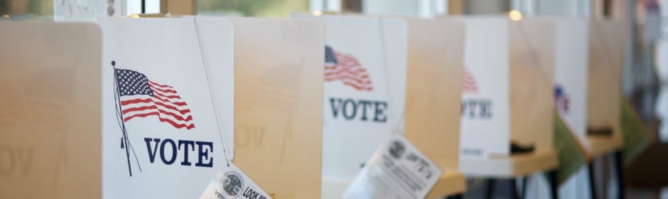 Row of voting booths with American flags and 'VOTE' signs at a polling place