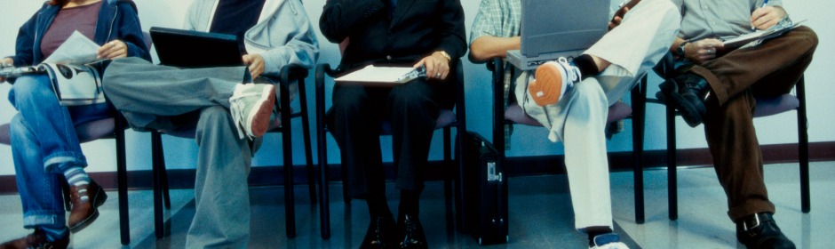 Row of people seated in chairs, each with laptops, notebooks, or papers, implying a recruitment or meeting setting.