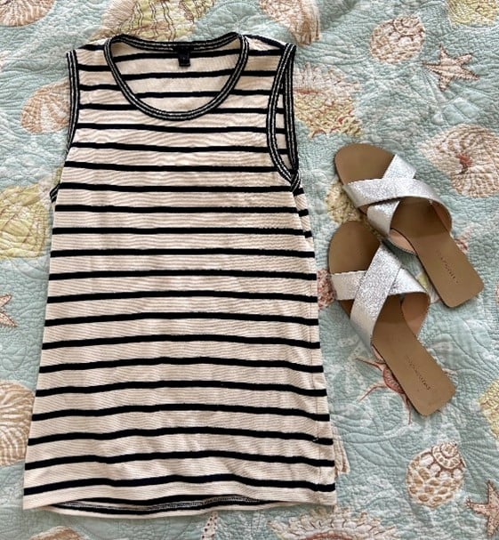 Striped sleeveless tank top with black stripes next to silver cross-strap sandals on a seashell-patterned quilt.