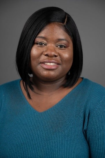 Portrait of a smiling woman wearing a teal knit sweater against a gray background.