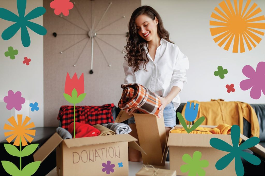 Young woman sorting donated clothes into boxes in a colorful, flower-decorated room.