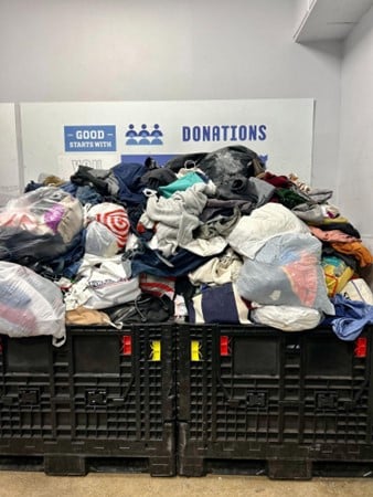 Piles of donated clothes stacked in black bins with a donations sign in the background.