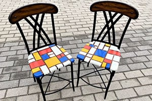 Two black metal chairs with colorful patchwork cushions on a cobblestone patio.