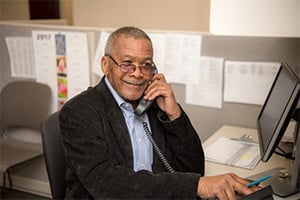Smiling older man in a blazer talking on a landline at his office desk