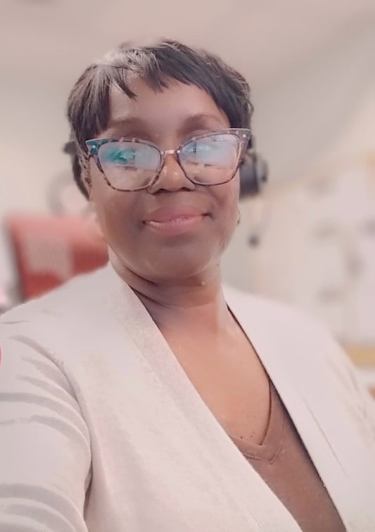 Portrait of a smiling woman wearing glasses and a light blazer.