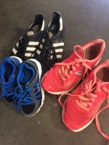 Blue and black athletic sneakers with blue laces, a black-and-white pair, and pink running shoes on a dark floor.