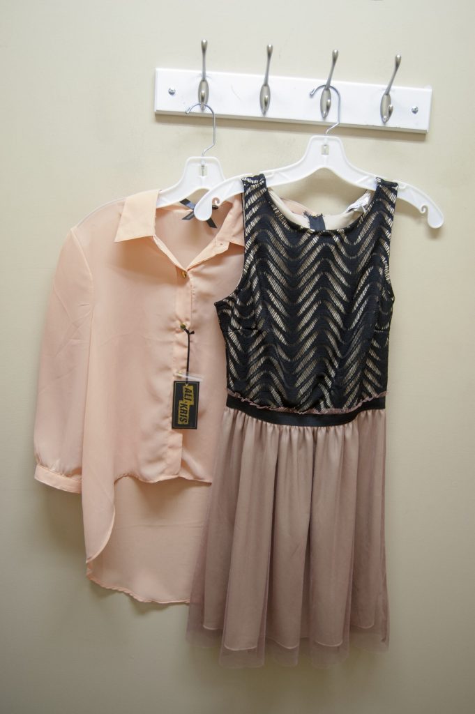 Peach chiffon blouse beside a black lace dress with a pink tulle skirt on hangers.