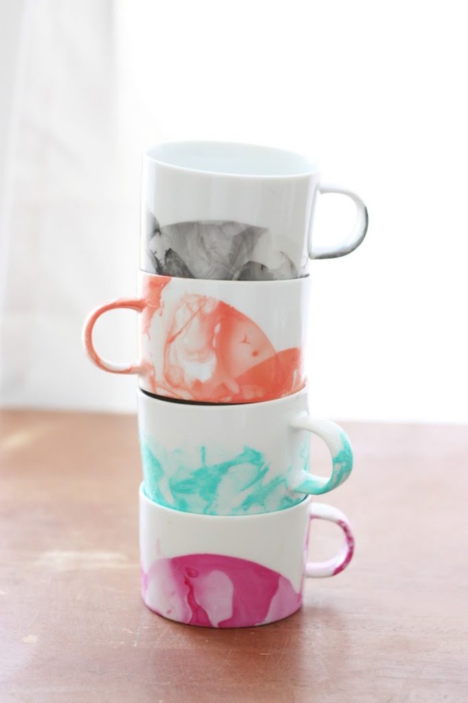 Stack of five ceramic mugs with marbled patterns in grayscale, coral, teal, and pink on a wooden table.