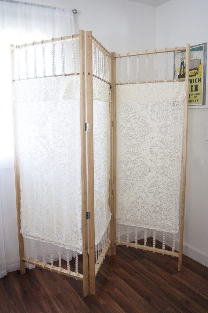 Wooden room divider with lace panels forming privacy screens in a bright room.