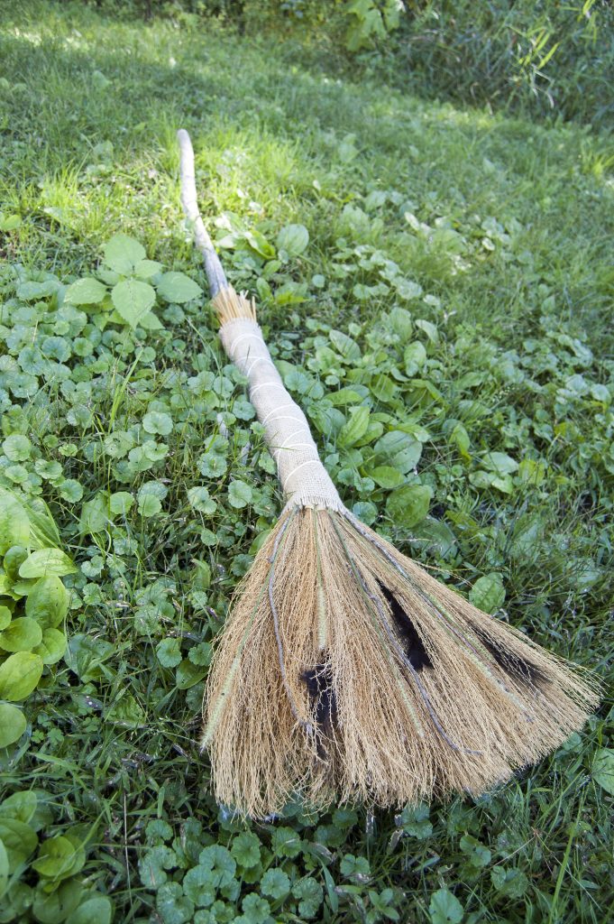 Long straw broom with a wrapped handle lying among green groundcover.