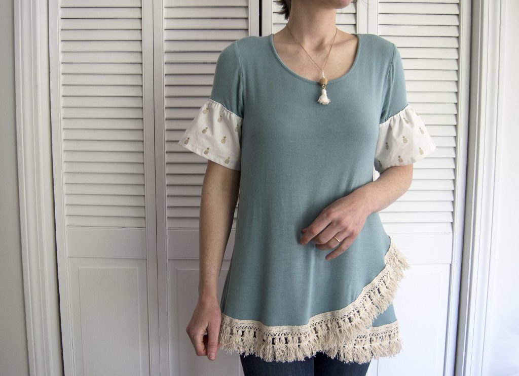 Woman wearing a teal tunic with white printed puff sleeves and a fringed hem, indoors.