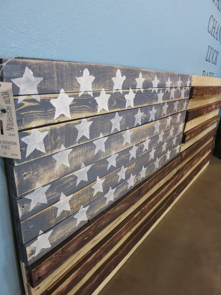 Weathered wooden planks with white stars arranged like a flag, stacked against a light blue wall.