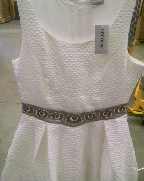 White textured sleeveless dress with a geometric black belt on display.