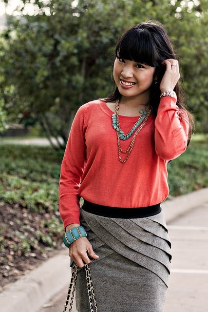 Smiling woman wearing coral sweater and layered turquoise necklaces outdoors.