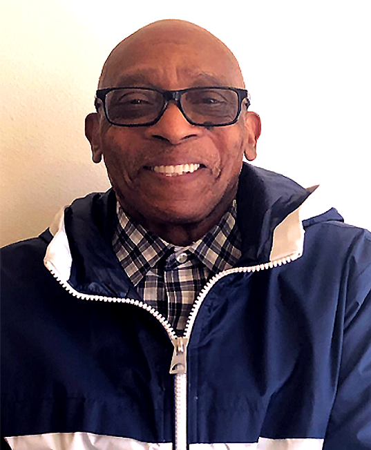 Smiling man wearing glasses and a navy windbreaker over a plaid shirt.