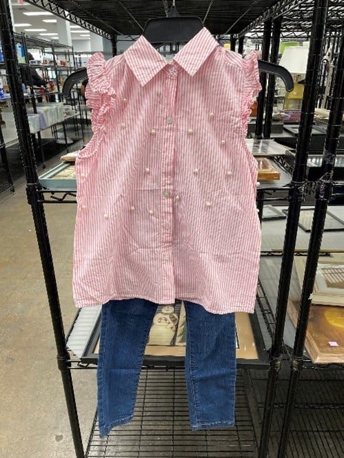 Pink and white striped sleeveless blouse with ruffled armholes, displayed on a hanger with blue denim jeans.
